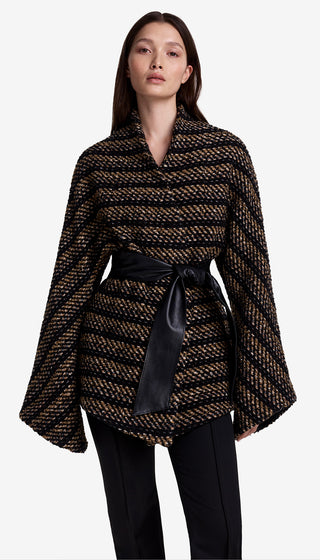 Woman wearing a patterned poncho with a black belt against a white background