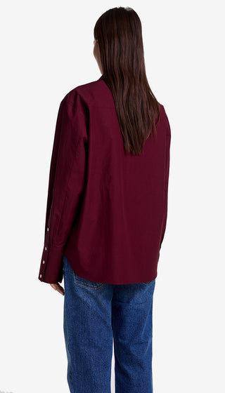 Person wearing a burgundy jacket and blue jeans on a white background