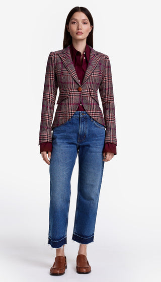 Woman wearing a plaid blazer, red shirt, blue jeans, and brown shoes on a white background