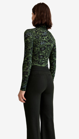 Person wearing a green camouflage long-sleeve top with black floral patterns and black pants on a white background