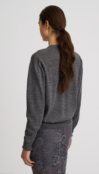 A woman shown from the back wearing a dark gray heathered long-sleeve crewneck sweatshirt and a dark gray lace skirt, against a plain light gray studio background.