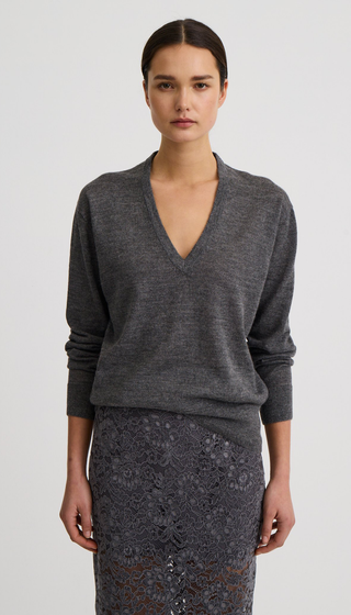 A model wearing a dark gray v-neck knit sweater and a matching dark gray lace skirt, photographed against a light gray studio background.