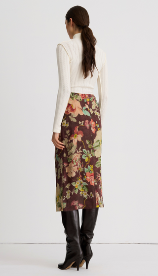 A model shown from the back wearing a cream ribbed mock-neck top, a brown floral midi skirt, and black knee-high boots, against a plain white studio background.