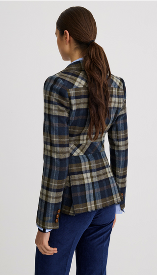 A woman shown from the back wearing a navy, brown, and beige plaid blazer with dark blue trousers, photographed against a light gray studio background.