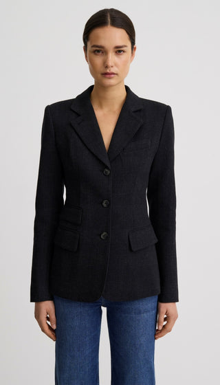 A woman modeling a dark navy blue tailored blazer with three front buttons, notched lapels, and flap pockets, paired with blue jeans against a light gray studio background.