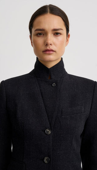 A woman wearing a dark charcoal gray textured jacket with a high mock neck collar and three front buttons, photographed against a light gray studio background.