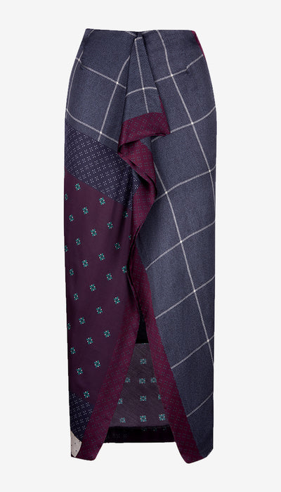 A wrap-style midi skirt featuring a navy blue and gray windowpane pattern on one side, a deep purple side panel with small teal floral motifs, and a solid purple front tie detail, shown against a plain light gray background.