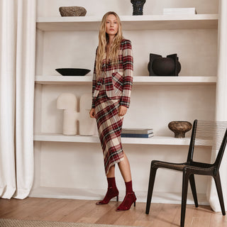 Woman in a plaid dress standing in a room with white shelves and a chair.