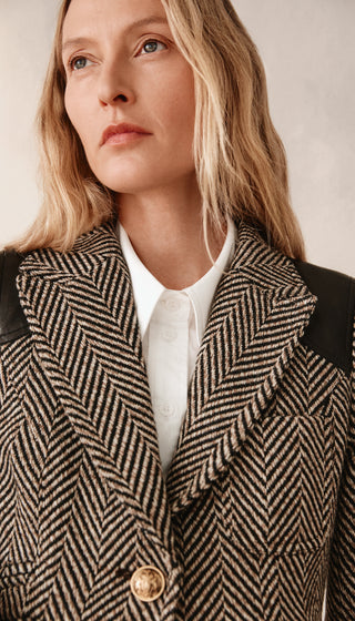 Woman wearing a herringbone patterned coat with a plain background