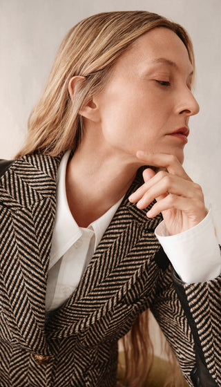 Person wearing a herringbone-patterned coat with a neutral background