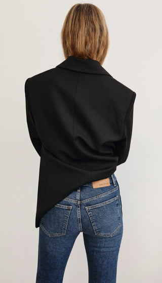 Person wearing a black jacket and blue jeans on a plain background