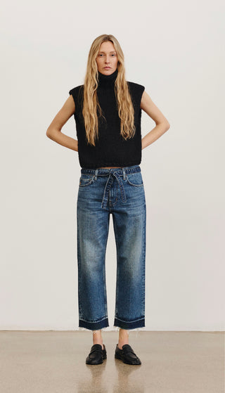 Woman wearing a black sleeveless top and blue jeans against a white background