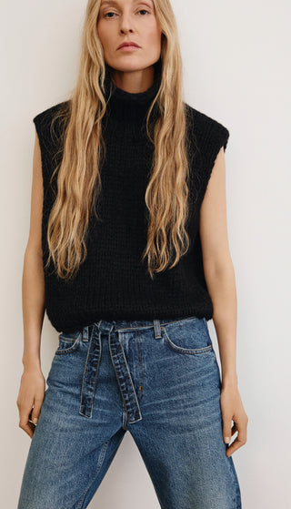 Woman wearing a black sleeveless top and blue jeans against a plain background