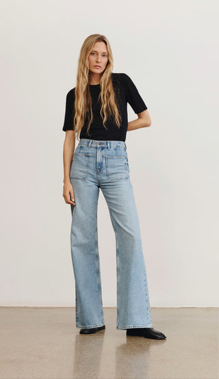 Woman wearing light blue jeans and a black top against a plain background