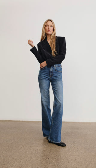 Woman wearing a black top and blue jeans against a plain background