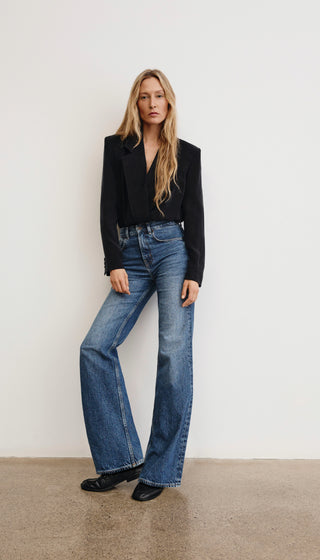 Woman wearing a black blazer and blue jeans against a white background