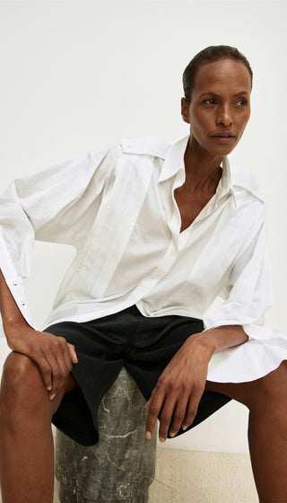 Person wearing a white shirt and black pants sitting on a stone block against a white background