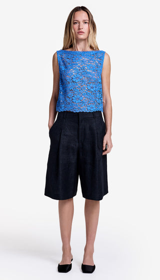 Woman wearing a blue lace top and black shorts on a white background