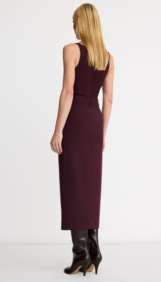 A woman shown from the back wearing a sleeveless, knee-length dark burgundy dress with a defined waist and black heeled ankle boots, photographed against a clean white studio background.