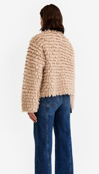 Person wearing a beige textured sweater and blue jeans on a white background