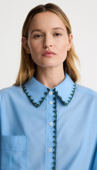 Woman wearing a light blue shirt with green trim on a white background
