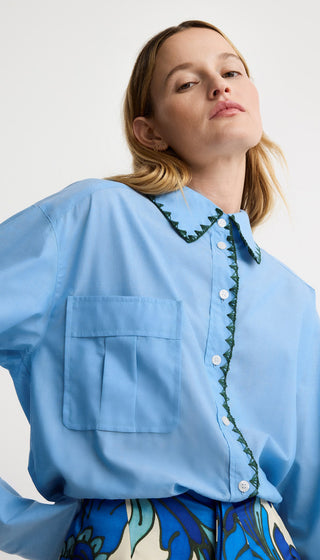 Woman wearing a light blue shirt with green trim on a white background