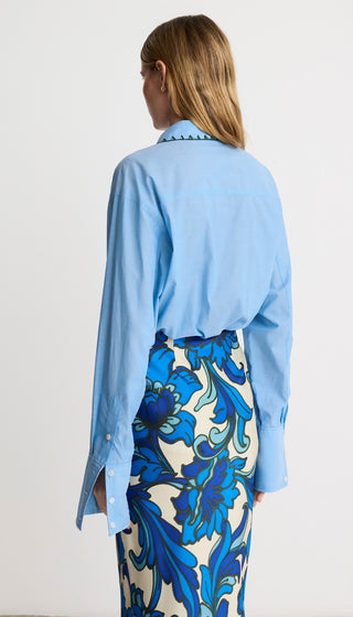 Woman wearing a light blue shirt and a blue floral skirt on a white background