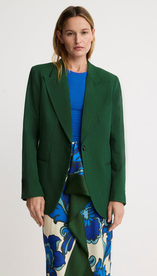 Woman wearing a green blazer over a blue top and floral pants on a white background